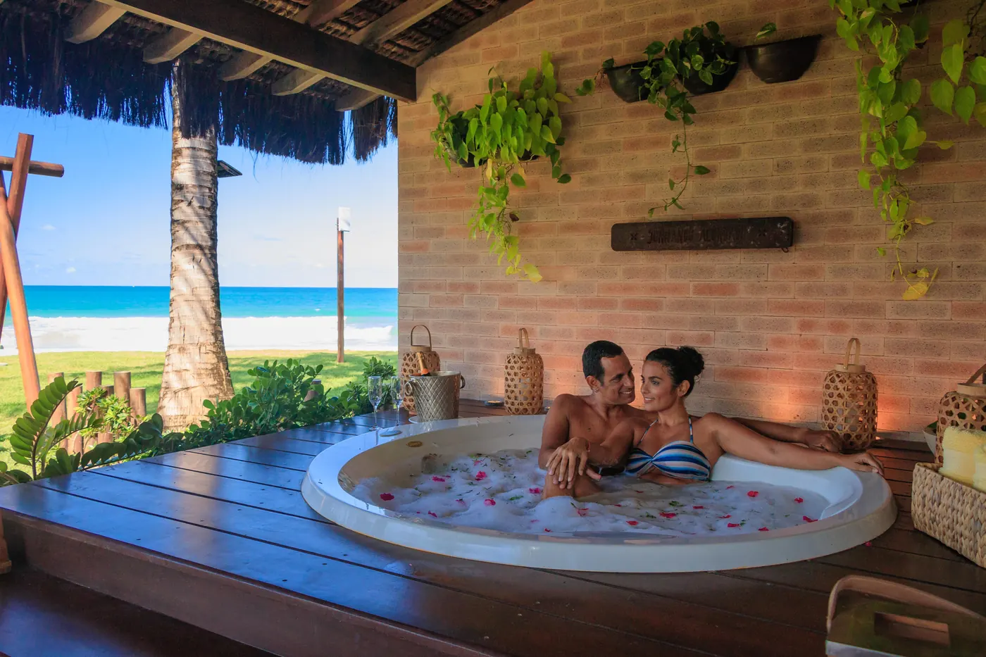 Casal na hidromassagem da varanda do bangalô, com o mar ao fundo